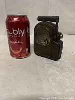 Camera size comparison with a standard 12oz sparkling water can, showing its compact size.