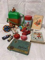 Overview photo showing various vintage collectibles, tins, toys, and paper items arranged on white cloth background.