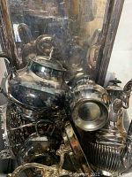 Photo showing silver plated teapot, sugar bowl, creamer, and serving tray with reflective surfaces and detailed edges.