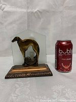 Front view of Art Deco desk lamp with copper-toned cast iron base, frosted glass panel, greyhound motif; soda can for scale