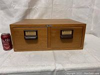 Front view of the oak card file cabinet with two drawers and label holders alongside a can for scale.