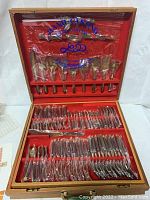 Full view of the entire open teak case showing all flatware and serving pieces arranged in the red velvet-lined slots.