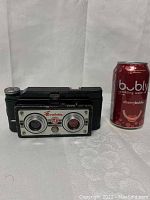 Front view of camera next to a soda can for scale.