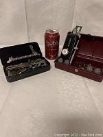 Two sewing machine accessory cases and a soda can for size. One case is black filled with various metal parts, the other is burgundy, containing Singer brand attachments.