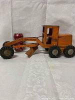 Overall side view of vintage orange Tonka road grader with one soda can for size reference showing the grader blade and rubber tires.