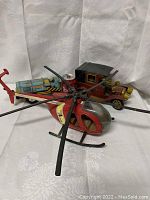 Photo showing red metal helicopter in front, with vintage tin toy truck and red toy car behind.