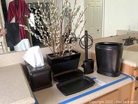 Bathroom vanity set displayed on countertop showing tissue holders, trays, waste basket, towel stand, and floral arrangement.