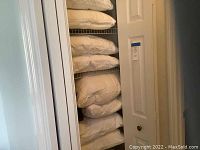 Closet shelf filled with stacked white bed pillows