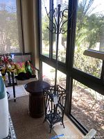 Photo of black metal coat stand near sunlit window beside drum style side table and chair.