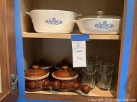 Lower shelf showing four brown onion soup bowls with lids and handles, and six clear medium-sized drinking glasses.