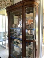 Full front view showing curved wood frame, glass doors, shelves, and interior lighting.