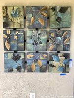 Front view of the nine connected square wooden panels displaying stylized botanical designs with leaves and branches in blue, gold, and black on a textured background.