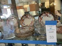 View of dessert plates stacked with six cut-glass aperitif glasses in front, inside glass cabinet.