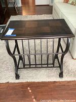 Front and side view of the wood and metal end table showing curved metal legs and the integrated magazine rack underneath, placed on carpet.