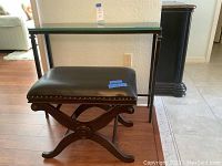 Side view of leather bench with dark wooden curved legs and brass tack trim on black leather seat cushion.