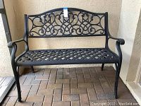 Front view of a black metal garden bench with curved armrests and intricate scrollwork on backrest.