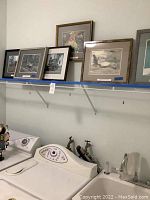 Photo showing framed and matted international photography prints displayed above a washing machine in a laundry room.