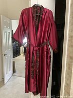 Full-length front view showing the deep red satin fabric, kimono style wide sleeves, collar and brocade belt tied at waist