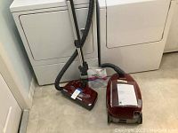 Canister vacuum, hose, wand and floor head arranged on tile floor