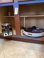 Two kitchen appliances side by side on a shelf: Waring Pro waffle maker on the left and Zojirushi electric griddle on the right, with lid on.