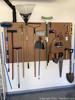 Full view of the tools hanging on a pegboard in garage showing the variety of large and small hand tools, garden rakes, brooms and shovel