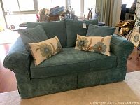 Front view of aqua colored textured fabric love seat with two floral decorative pillows placed on seat cushions.