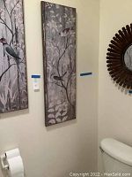 Two vertical painted wood planks with birds on branches hung on a wall above a toilet paper holder