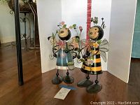 Two metal bumblebee figurines, 16 inches tall, on springs placed on wooden floor with white background and red measurement scale visible.