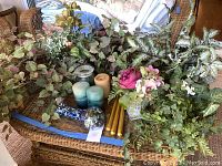 Wide shot showing silk flower vines and bouquet on wicker chair with candles and blown glass fish art piece on blue tray