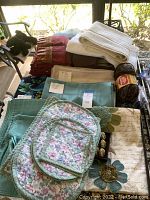 Overview photo showing folded towels, placemats, and table linens on a glass table outdoors with some floral and geometric patterns.