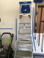 Front view of the 6-foot aluminum ladder extended with stepstool in front, hanging on garage wall with other tools.