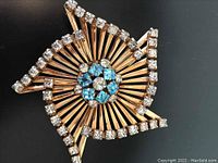 Full front view of gold filled pinwheel brooch showing aqua square rhinestones in center and clear rhinestones outlining pinwheel edges.