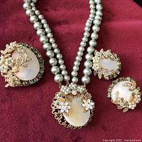 Photo showing matching necklace, two clip-on earrings, and a pendant or brooch on burgundy cloth.