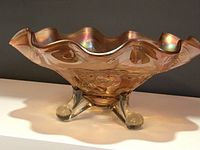 Side view of ruffled edge amber carnival glass bowl on three clear claw feet showing reflective iridescent surface