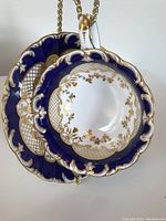 Photo of tea cup and matching saucer showing blue cobalt bands with gold ornate leaf and lattice patterning, scalloped rims