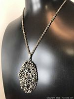 Front view of the Coro necklace displayed on black mannequin, showing detailed floral filigree pendant and chain length