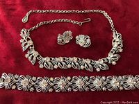 Photo of the full Coro set including necklace, bracelet, and earrings on red background