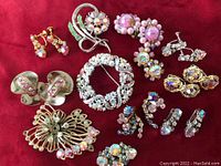 Full lot of 4 brooches and 8 pairs of earrings arranged on red background showing rhinestone colors and styles.