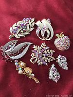 Full lot of red rhinestone costume jewelry on red fabric background showing 6 brooches and a pair of earrings.