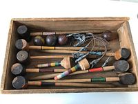 Top-down photo of the croquet set inside the wooden case showing mallets, balls, wire wickets, and goal pegs.