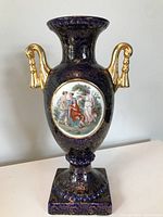 Full front view of cobalt blue urn showing gold floral design, gold handles, and classical scene medallion.