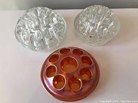 Three vintage flower frogs together on a white surface, two clear glass and one copper-colored metal.