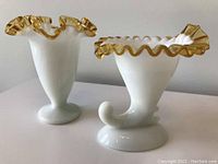 Two white milk glass vases with gold ruffled trim around the top, shown side by side on a white surface.