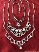 Lot of three blue aurora borealis rhinestone necklaces of varying lengths on a red background.