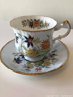 Teacup and saucer showing the overall floral Ming pattern with gold trim.