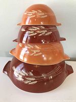 Stacked view of four Pyrex Cinderella mixing bowls in various brown and orange shades with Wheat pattern on the exterior.