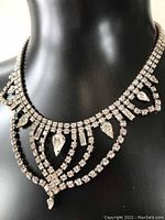 Front view of the rhinestone necklace displayed on a black mannequin, showing the overall design and drop accents.