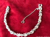 Full view of silver-tone tennis bracelet laid on red fabric showing clasp, safety chain, and length.