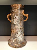 Front view of the tall ceramic vase showing abstract gold and brown design with female faces painted.