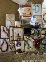 Full overview of assorted costume jewelry including necklaces, bracelets, earrings, and greeting cards laid out in boxes and bins